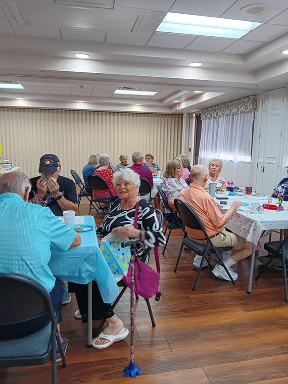 Members chatting at tables in the community center during Coffee, Tea and Chat
