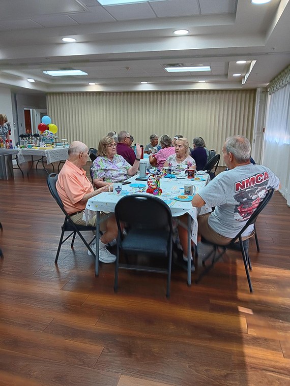 Residents seated around a long table at the Coffee, Tea and Chat birthday gathering