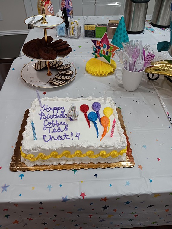 Sheet cake iced "Happy Birthday Coffee Tea & Chat 4" with cupcakes behind it
